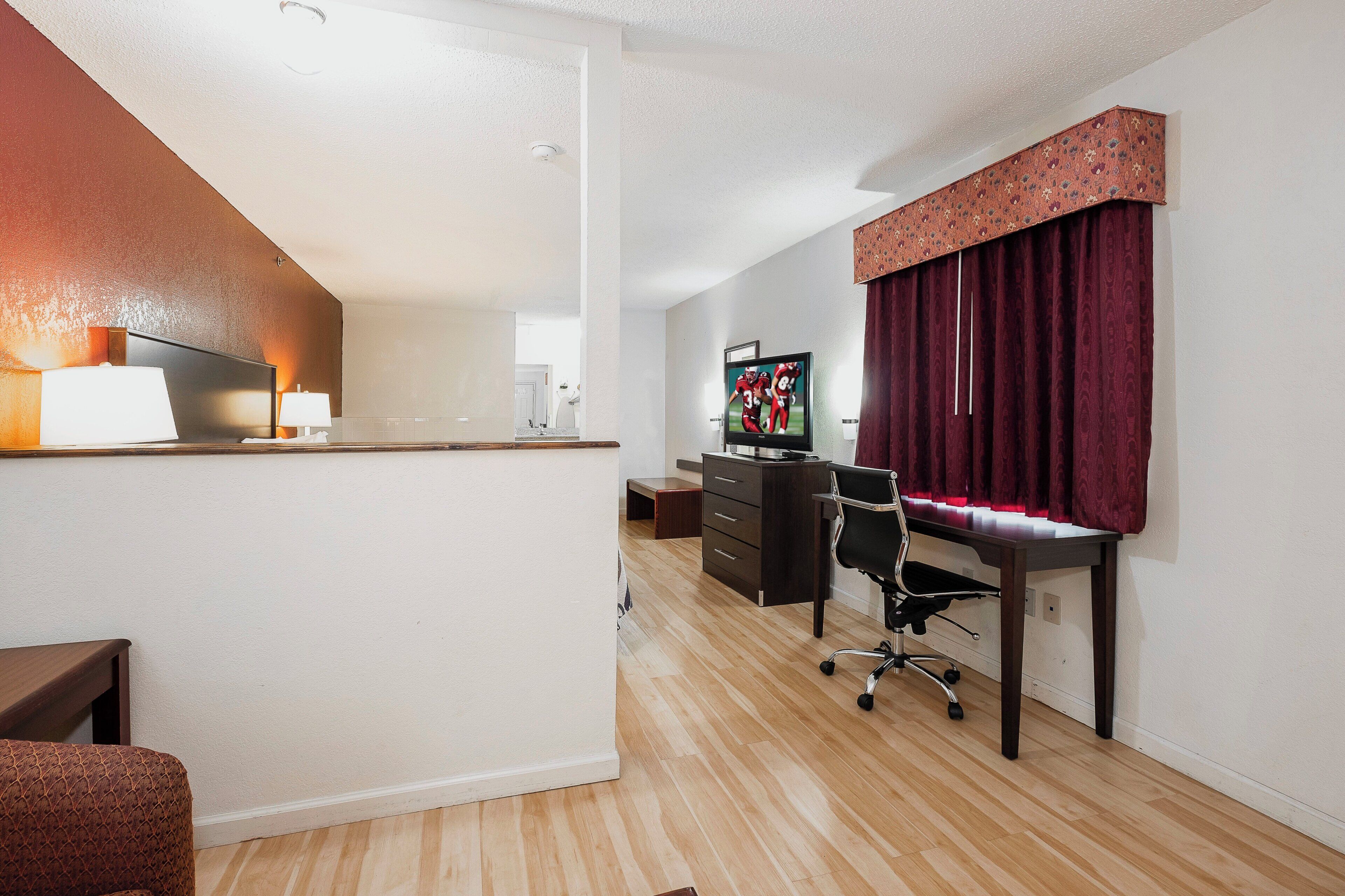 A hotel room with a desk, chair, TV, and a red curtain.