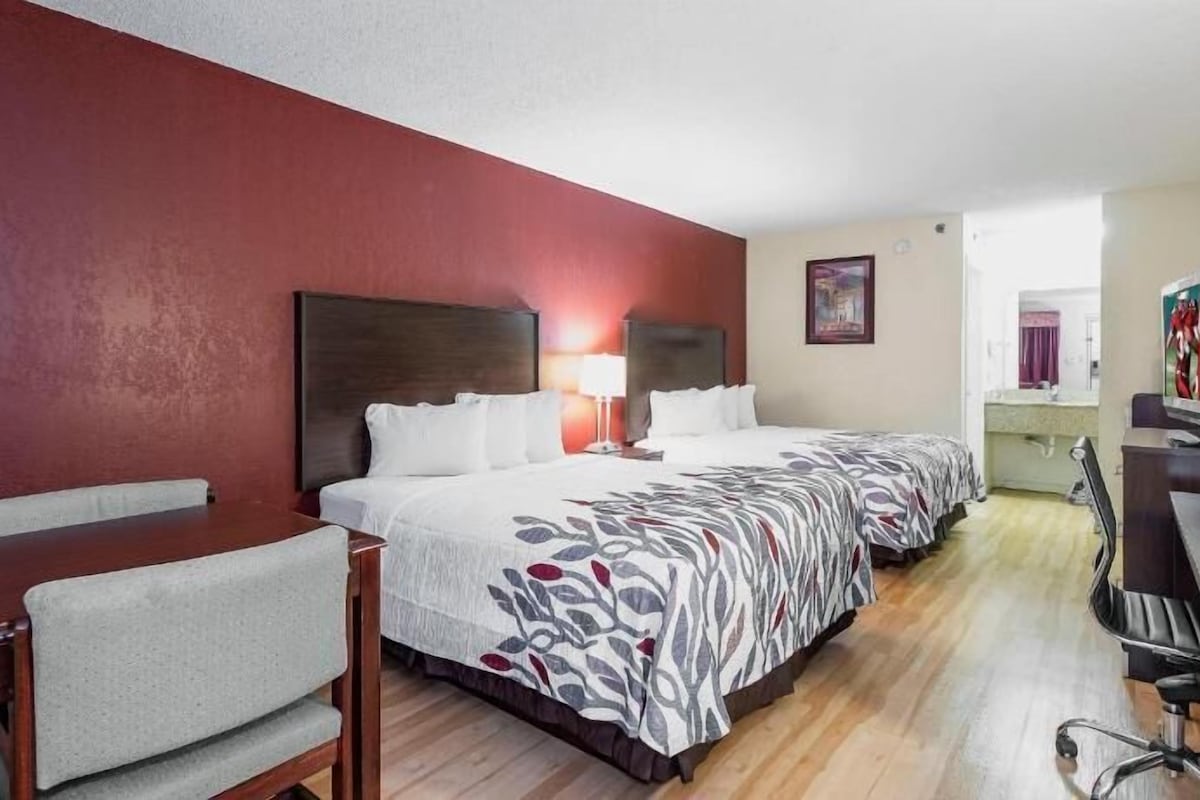 A hotel room with a large bed, a desk, a chair, a TV, and a bathroom.