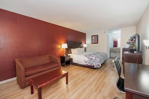 A hotel room with a bed, a sofa, a nightstand, a desk, and a television.