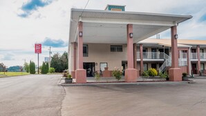 Un motel con zona de estacionamiento techada, un edificio de una sola planta y un pequeño espacio al aire libre para sentarse.