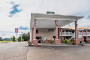 A motel with a covered parking area, a single-story building, and a small outdoor seating area.