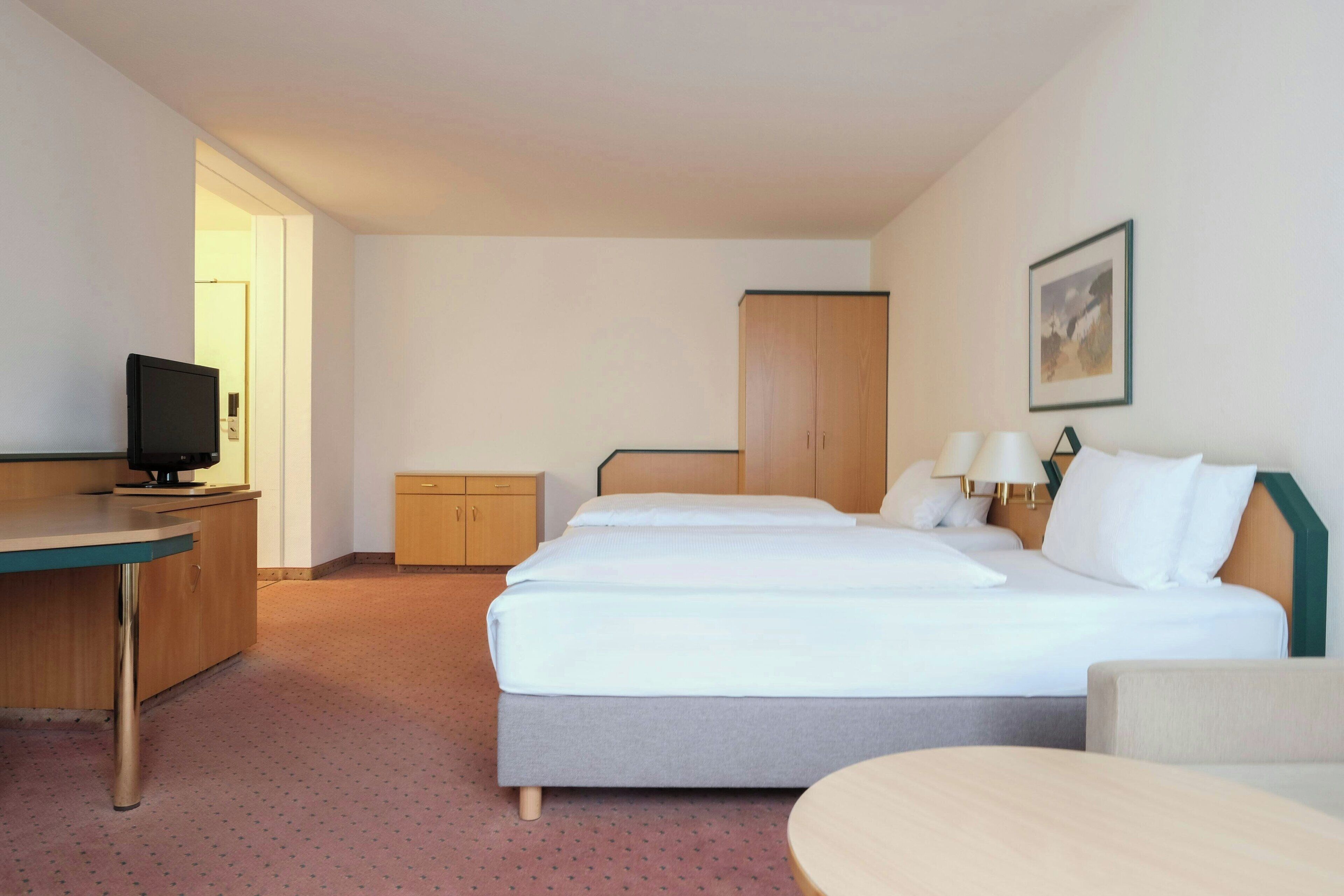 A hotel room with a bed, a desk, a television, a wardrobe, and a painting on the wall.