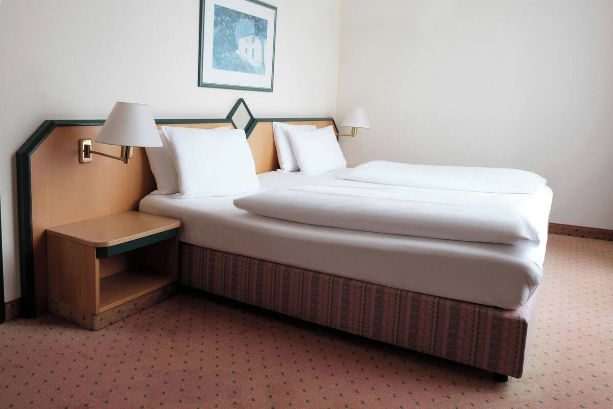 A hotel room with a bed, two bedside tables, and a framed picture on the wall.