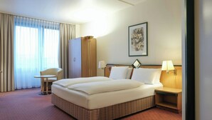 Une chambre d’hôtel avec un grand lit, un bureau, une chaise, une armoire et un tableau au mur.