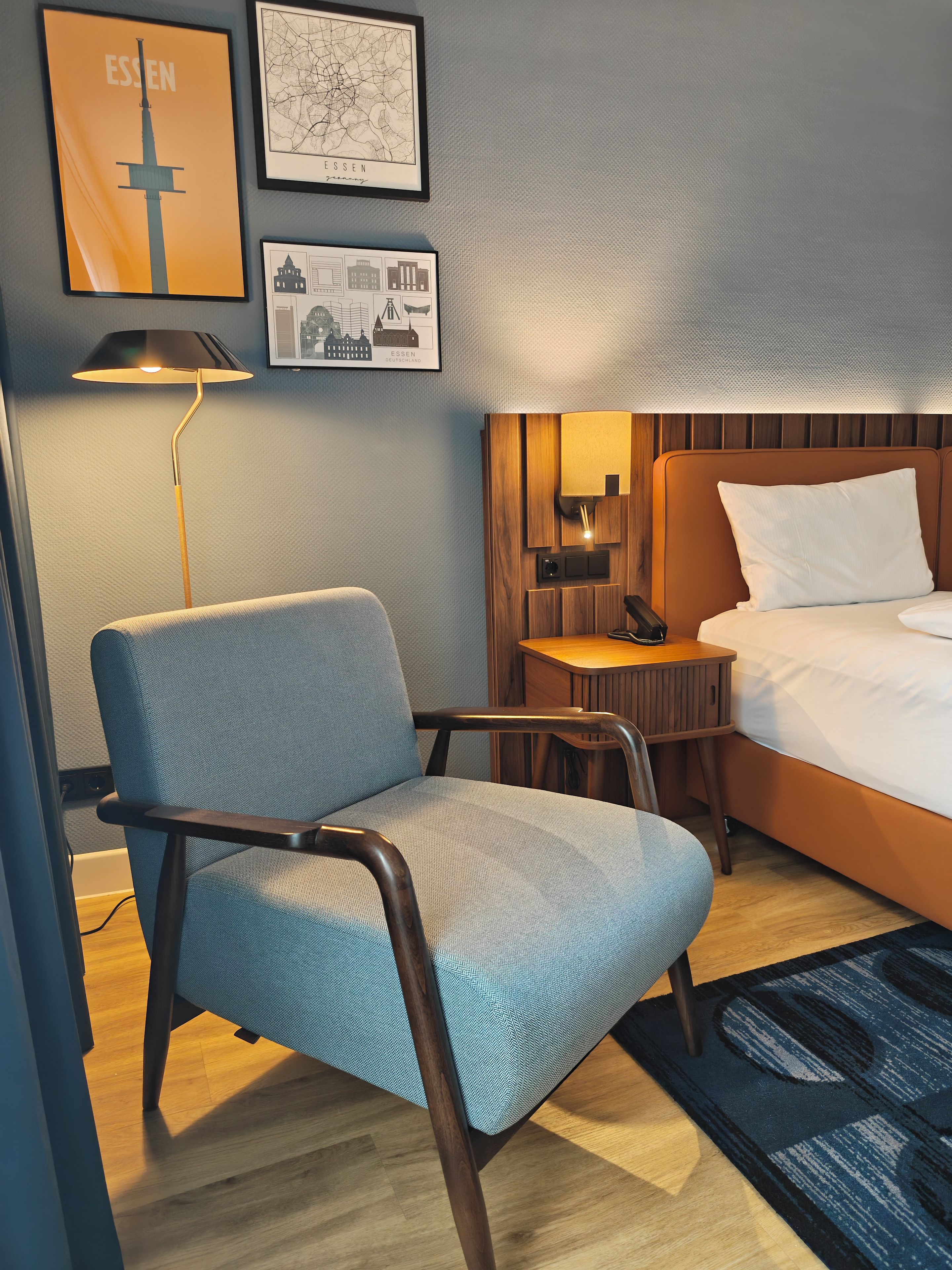 Une chambre d’hôtel équipée d’un lit, d’une chaise, d’un bureau et de lampes fixées au mur.
