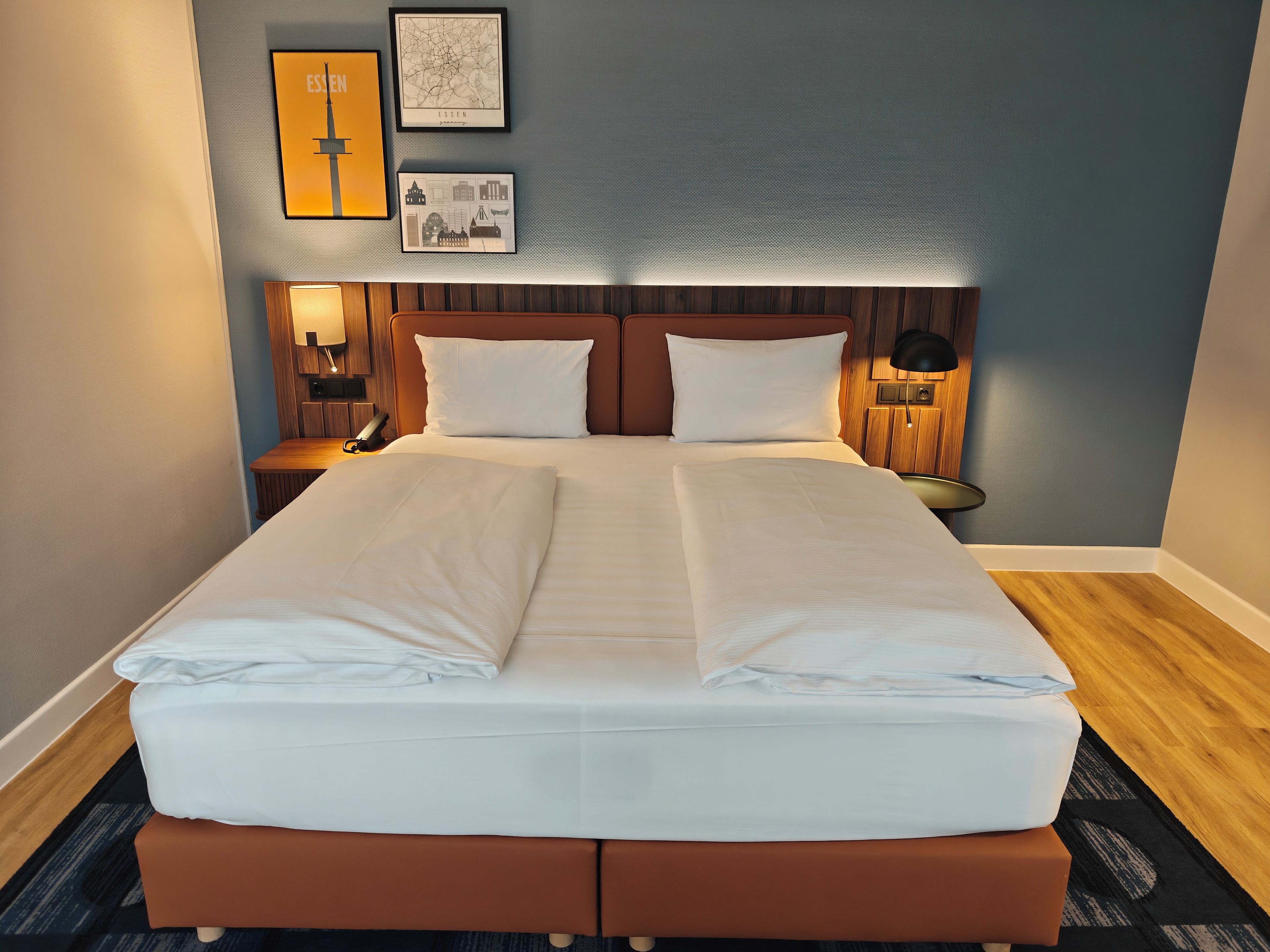 A neatly made double bed with a wooden headboard, two bedside tables with lamps, and framed pictures on the wall.