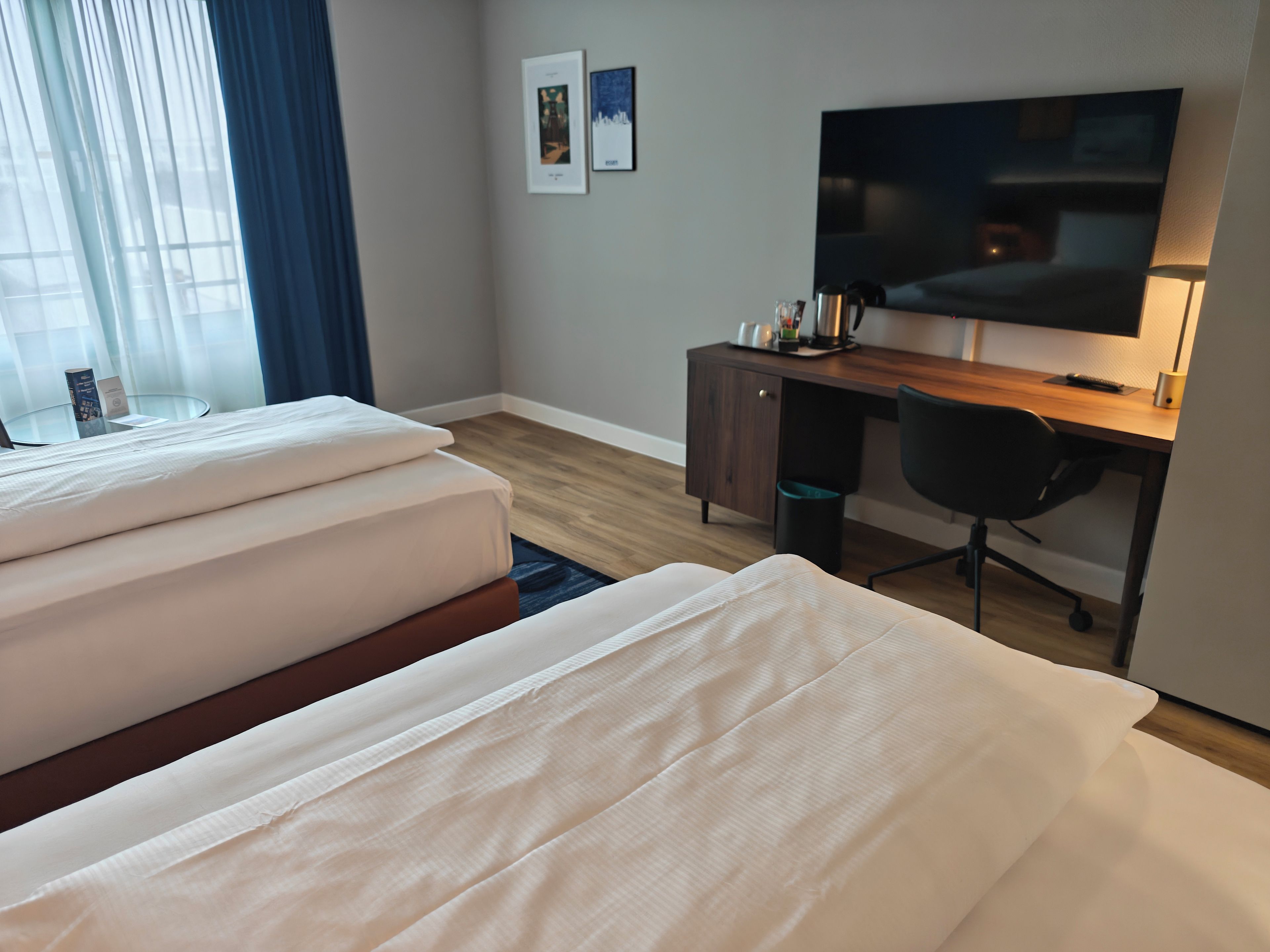 A hotel room with a bed, a desk, a chair, a television, and a window with curtains.