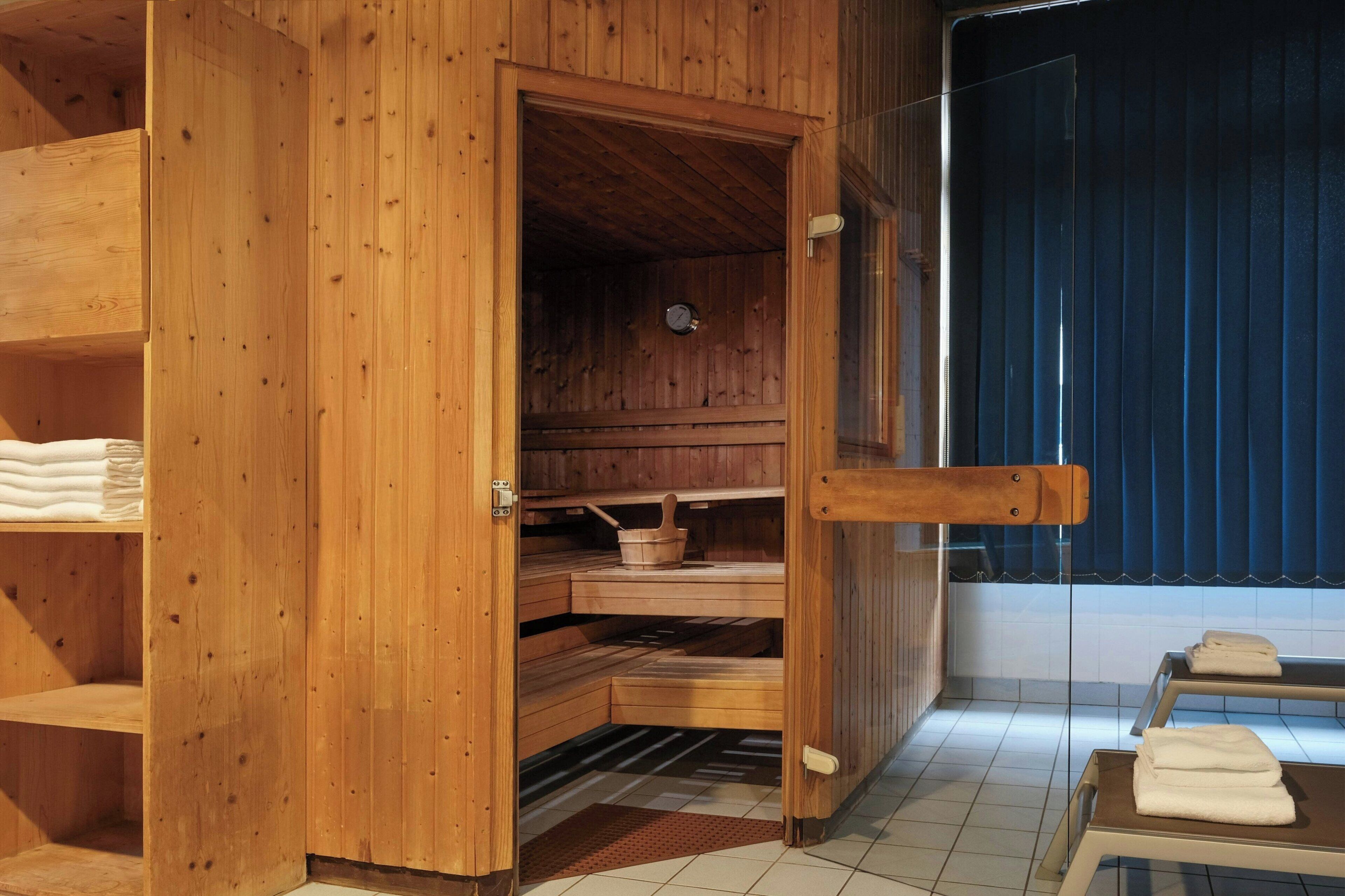 A wooden sauna room with a wooden bench, a small table with a bowl, and a clock on the wall.