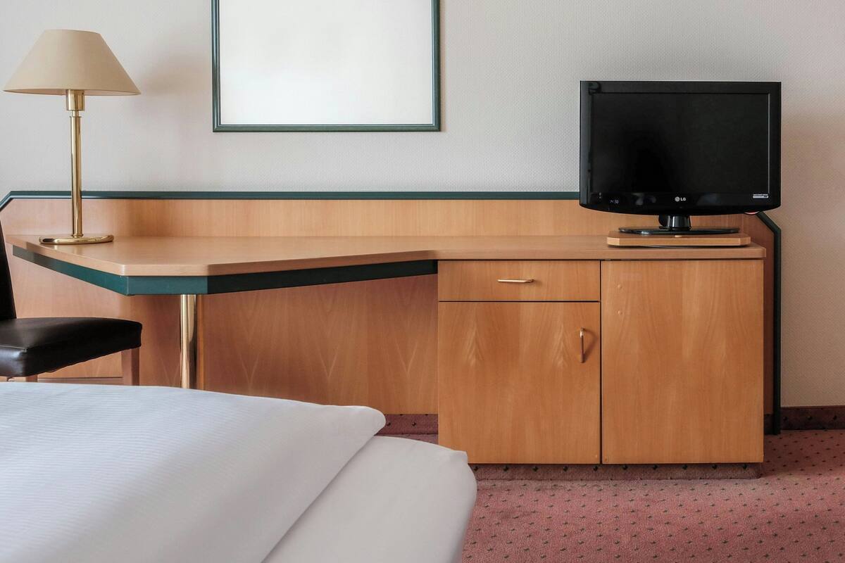 A hotel room with a bed, a desk with a television, a lamp, and a framed picture on the wall.