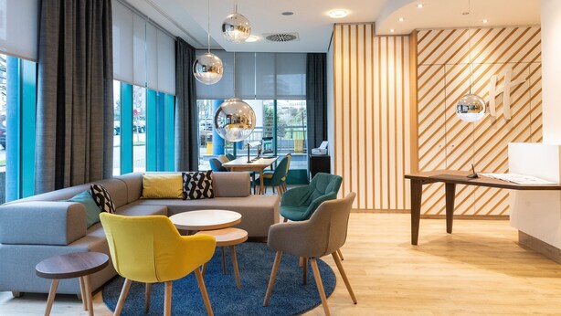 Un espace de détente moderne avec un canapé d’angle, un fauteuil jaune et une table ronde.