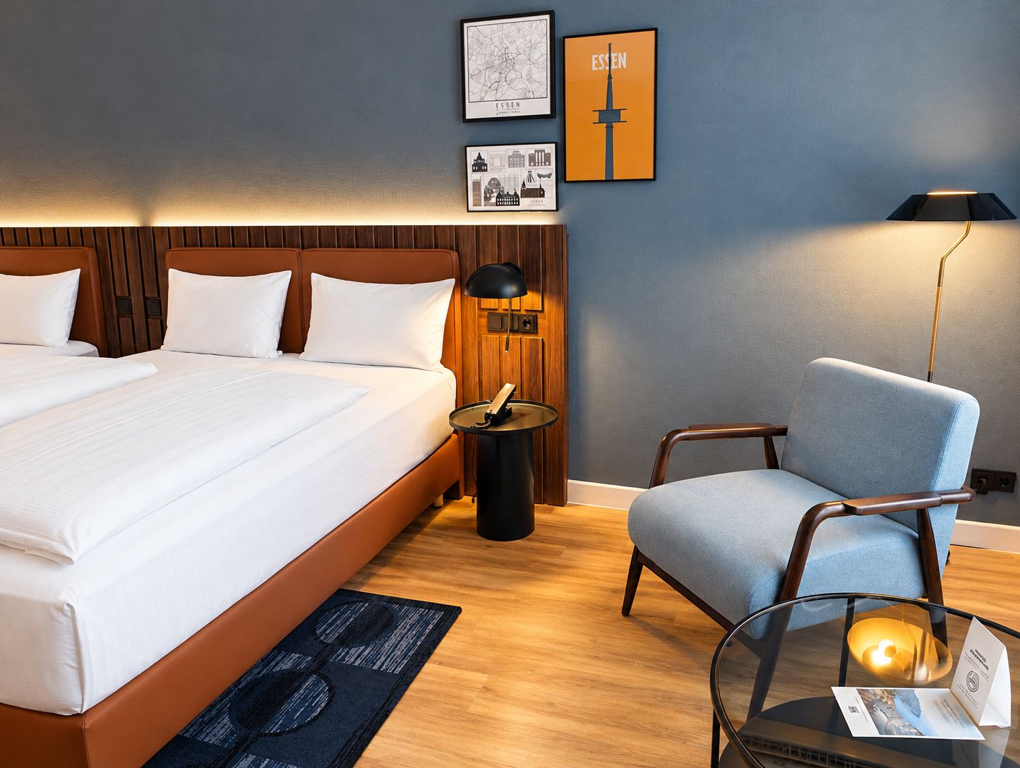 A hotel room with a large bed, a desk with a lamp, a chair, and framed pictures on the wall.