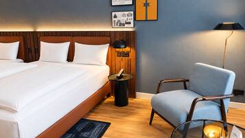 A hotel room with a large bed, a desk with a lamp, a chair, and framed pictures on the wall.