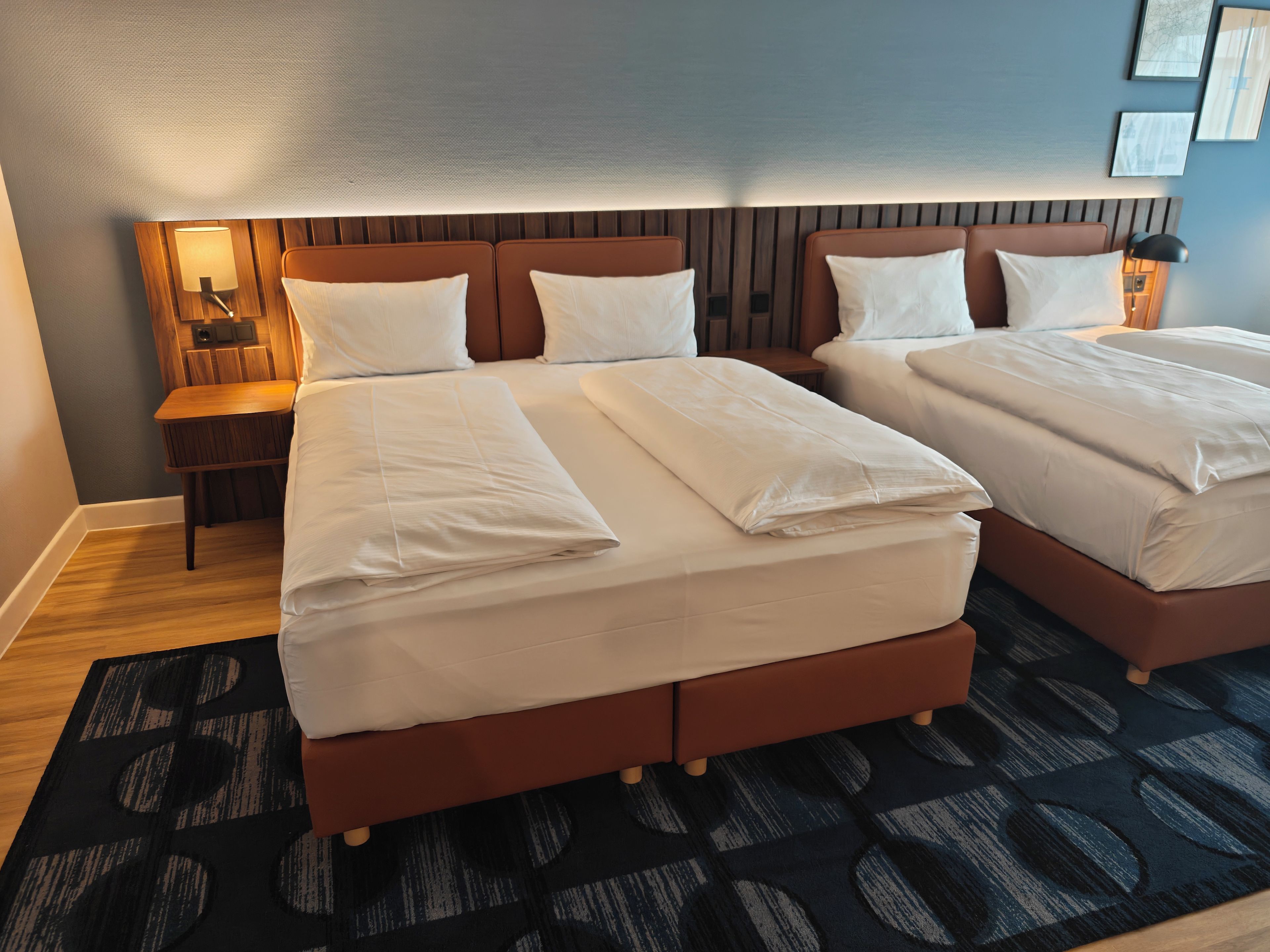 Une chambre d’hôtel avec deux lits, une table de chevet, une lampe et un tapis à motifs.