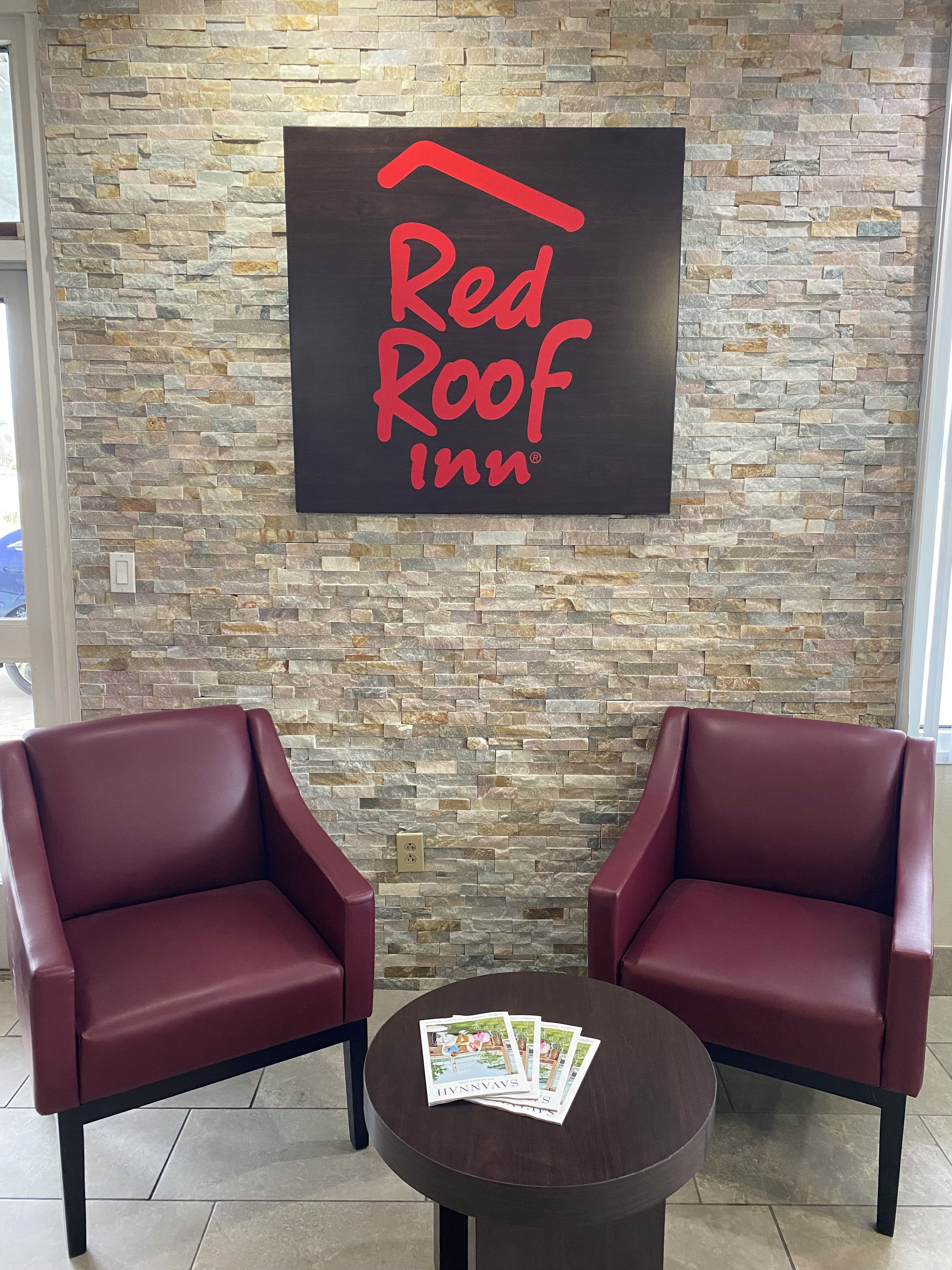 Une enseigne « Red Roof Inn » sur un mur de pierre, deux fauteuils en cuir rouge et une table avec des brochures.