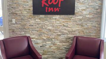 Une enseigne « Red Roof Inn » sur un mur de pierre, deux fauteuils en cuir rouge et une table avec des brochures.