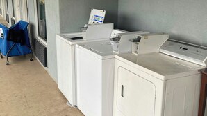 A laundry area with a row of washers and dryers, a blue cart, and a sign on the wall. - Red Roof Inn Savannah North I-95 – Port Wentworth (Port Wentworth)