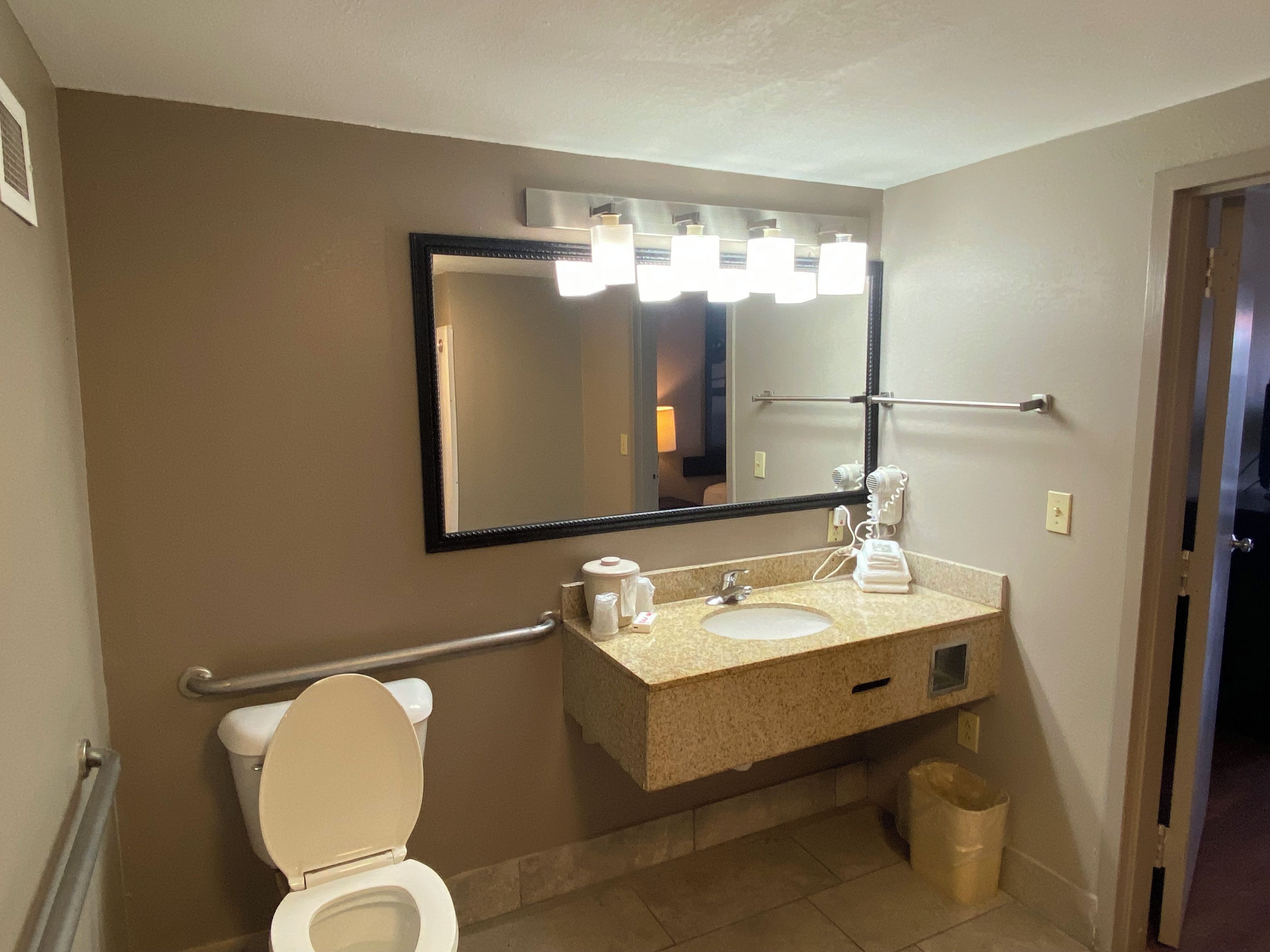 A bathroom with a toilet, sink, mirror, and towel rack.