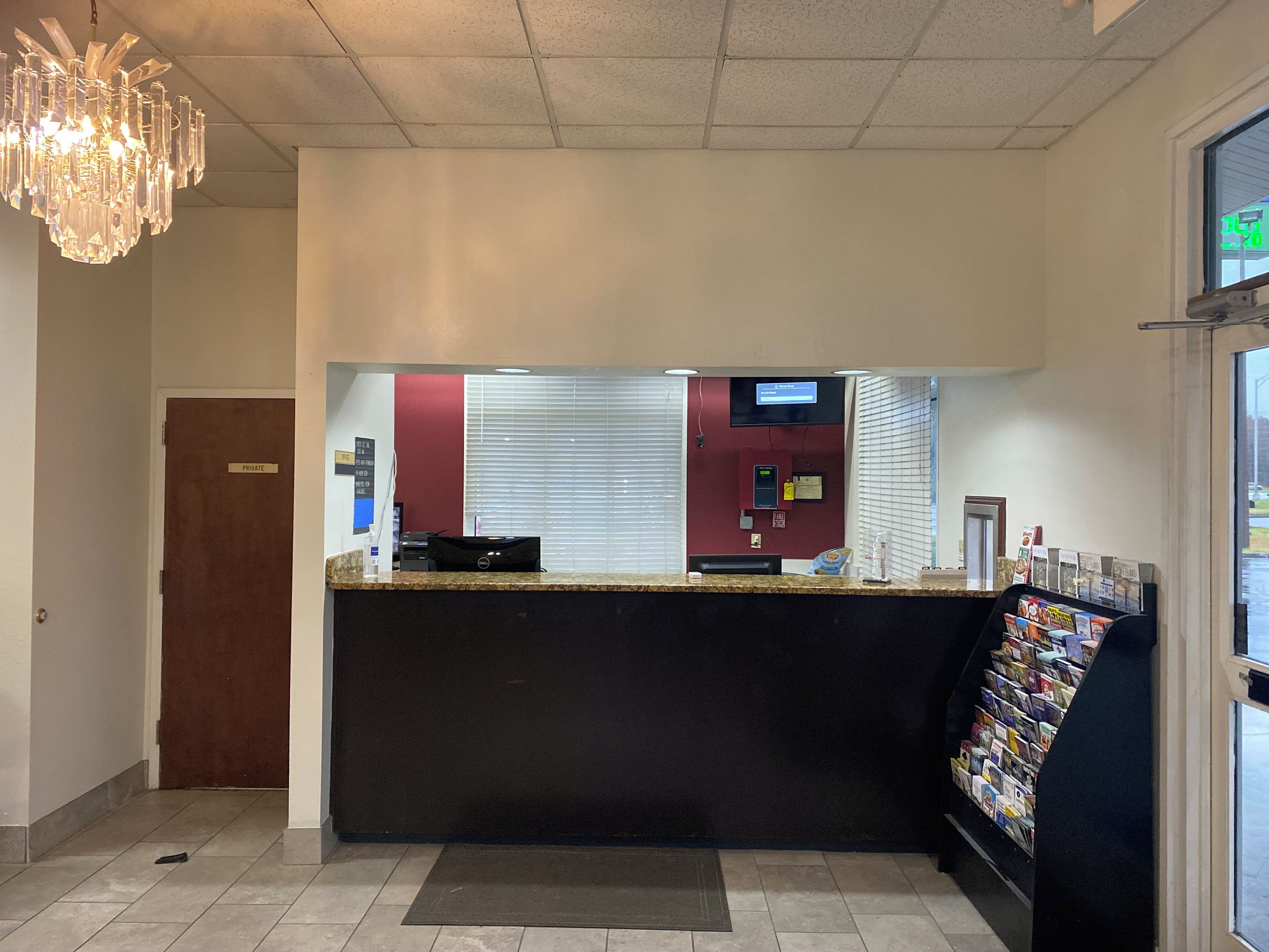 A hotel reception area with a reception desk, a private door, a digital screen, and a magazine rack.