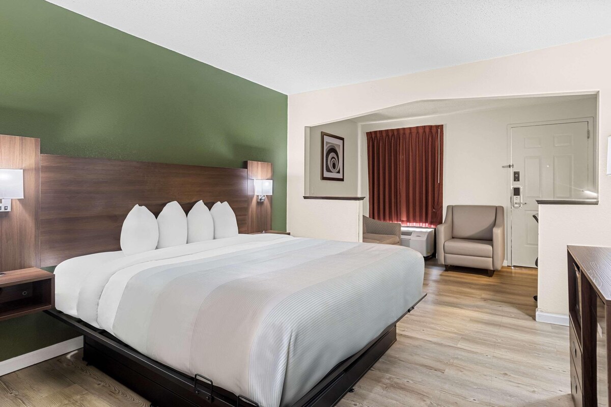 Habitación de hotel con una cama grande, un escritorio, una silla y una puerta que da a otra habitación.