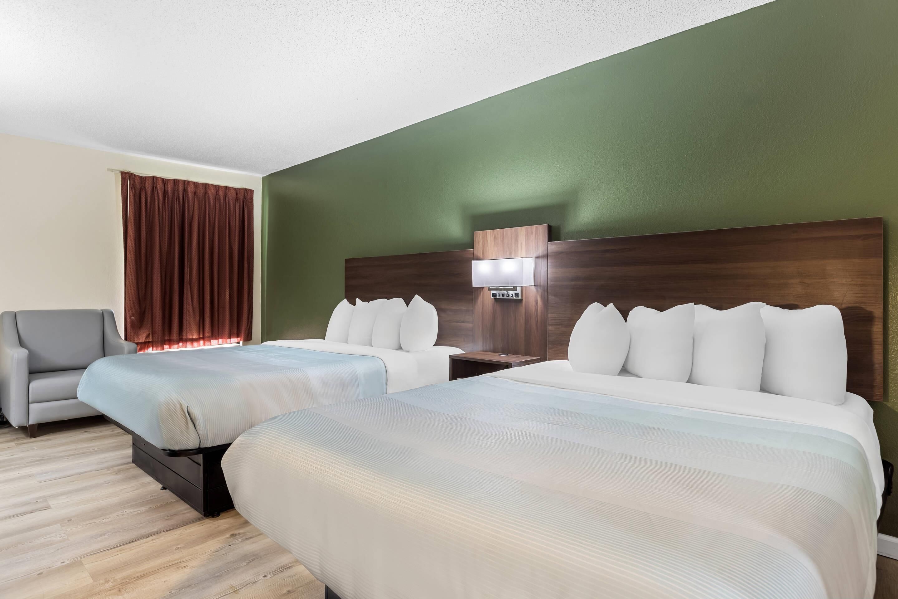 Une chambre d’hôtel avec deux lits, un canapé, une table de chevet et une lampe fixée au mur.