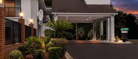 A modern hotel with a covered entrance, a satellite dish, and well-maintained landscaping.
