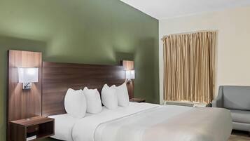 A hotel room with a large bed, two bedside tables with lamps, a grey armchair, and a window with curtains.
