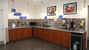 A modern kitchen with wooden cabinets, a microwave, coffee maker, and a refrigerator. There are signs for 'Hydrate' and 'Delight' on the wall. - Americas Best Value Inn Monroe (Monroe)