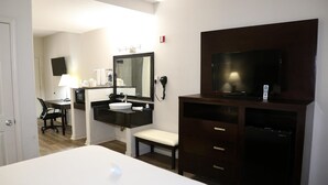A hotel room with a bed, a desk with a chair, a vanity with a mirror, a television, and a refrigerator. - Americas Best Value Inn Monroe (Monroe)