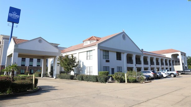 A two-story hotel with a red-tiled roof, a covered entrance, and a parking lot with several cars.