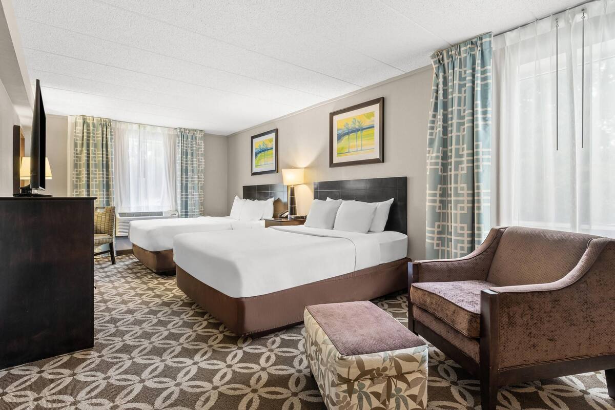 A hotel room with two beds, a desk, a chair, and a patterned carpet.