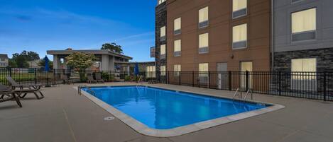 A swimming pool with a surrounding deck, a fence, and a building with a sign that reads "Comfort Suites."