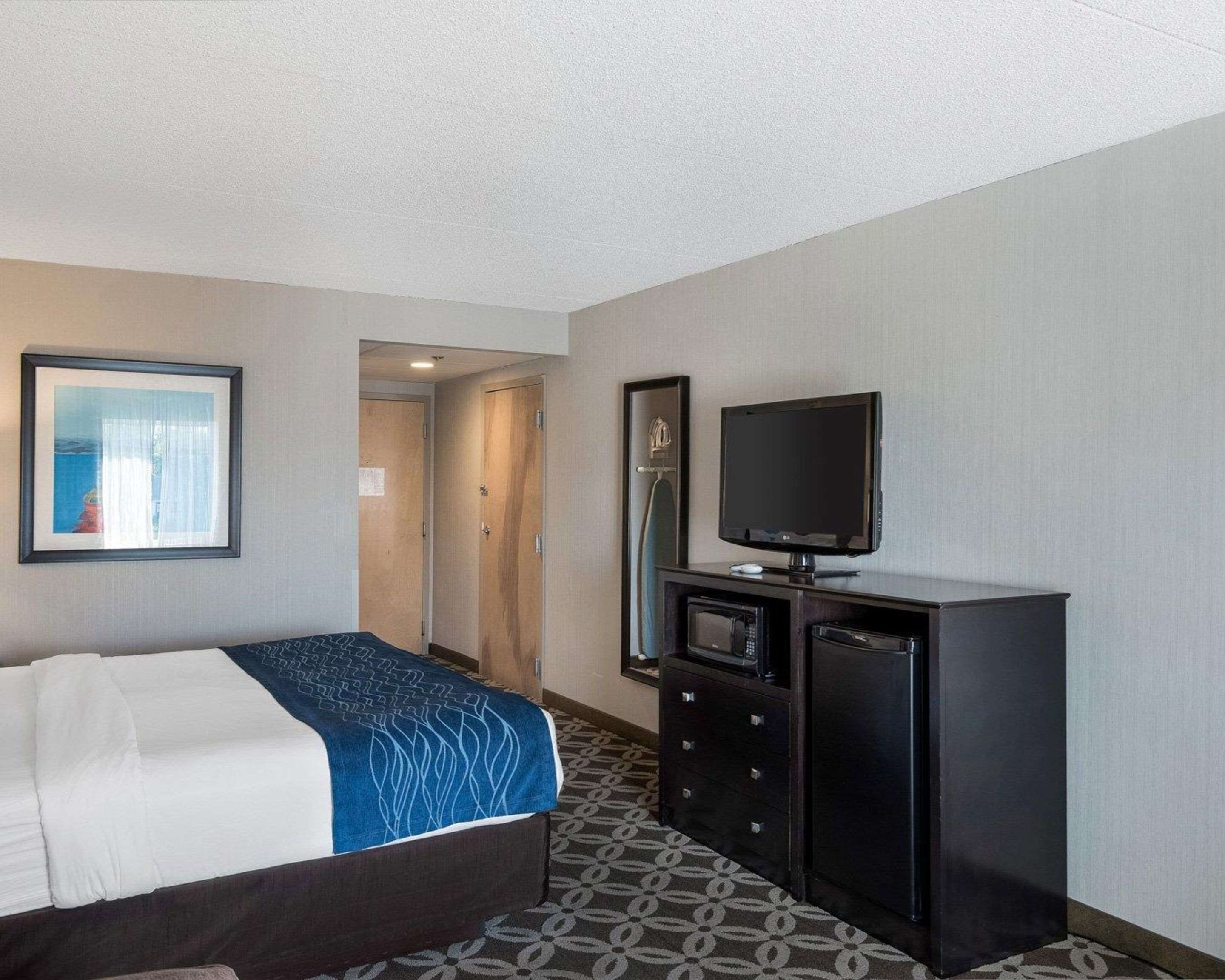 A hotel room with a bed, a television, a dresser, and a door leading to another room.