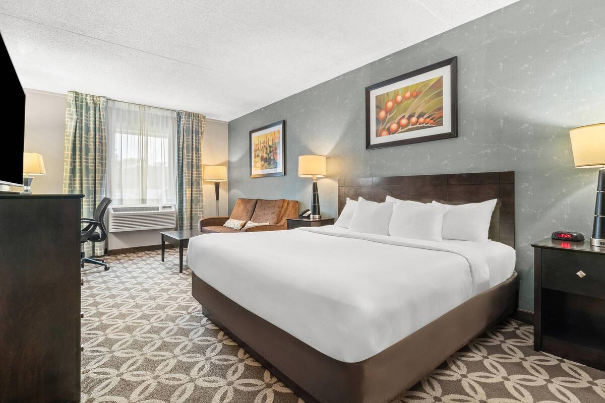 A hotel room with a large bed, a desk with a chair, two lamps, and a window with curtains.