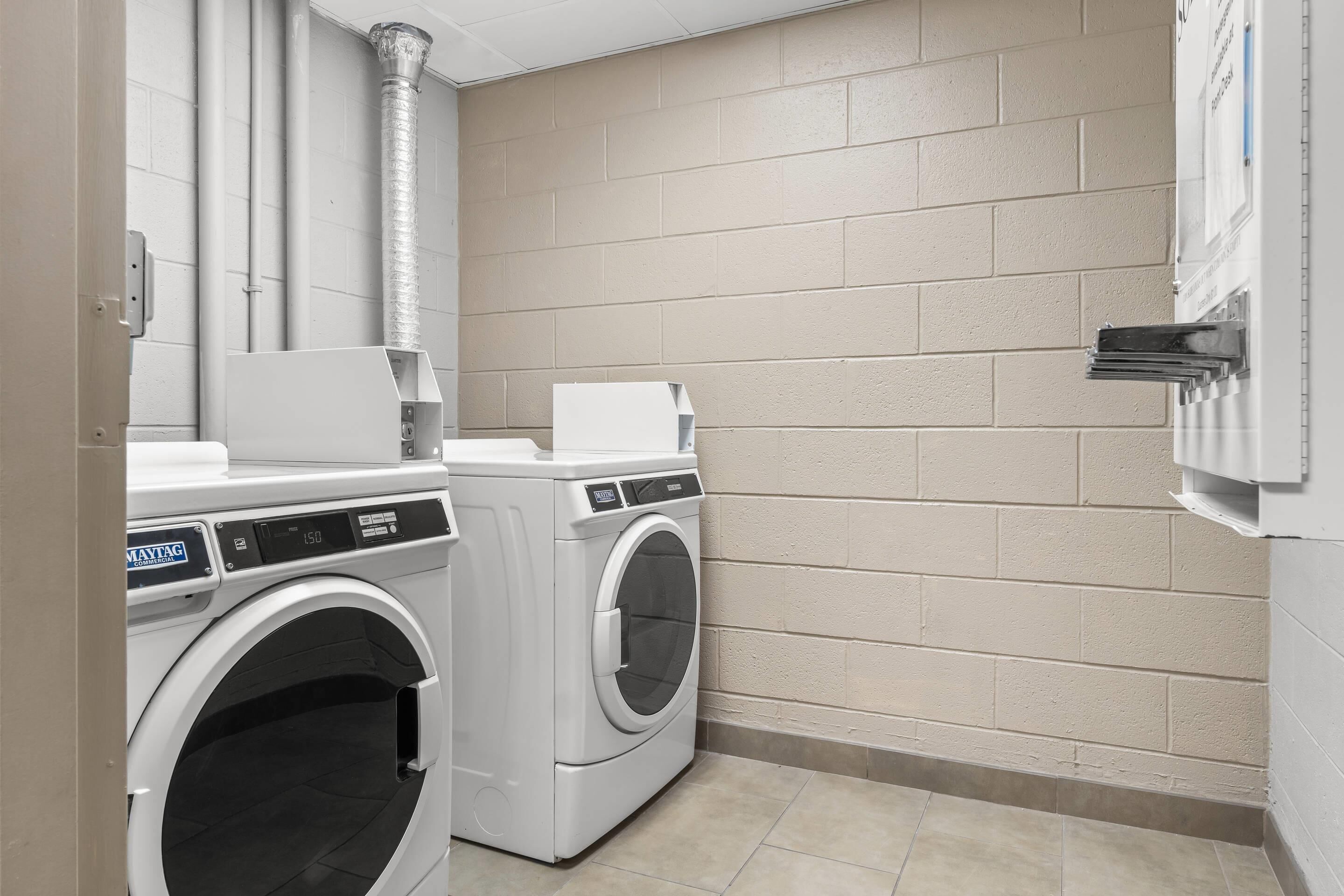 A laundry room with two front-loading washing machines, a dryer, and a ventilation system.