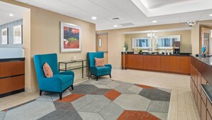 A modern hotel lobby with a reception desk, two blue armchairs, a patterned rug, and a large painting on the wall. - Comfort Inn Rehoboth Beach (Rehoboth Beach)