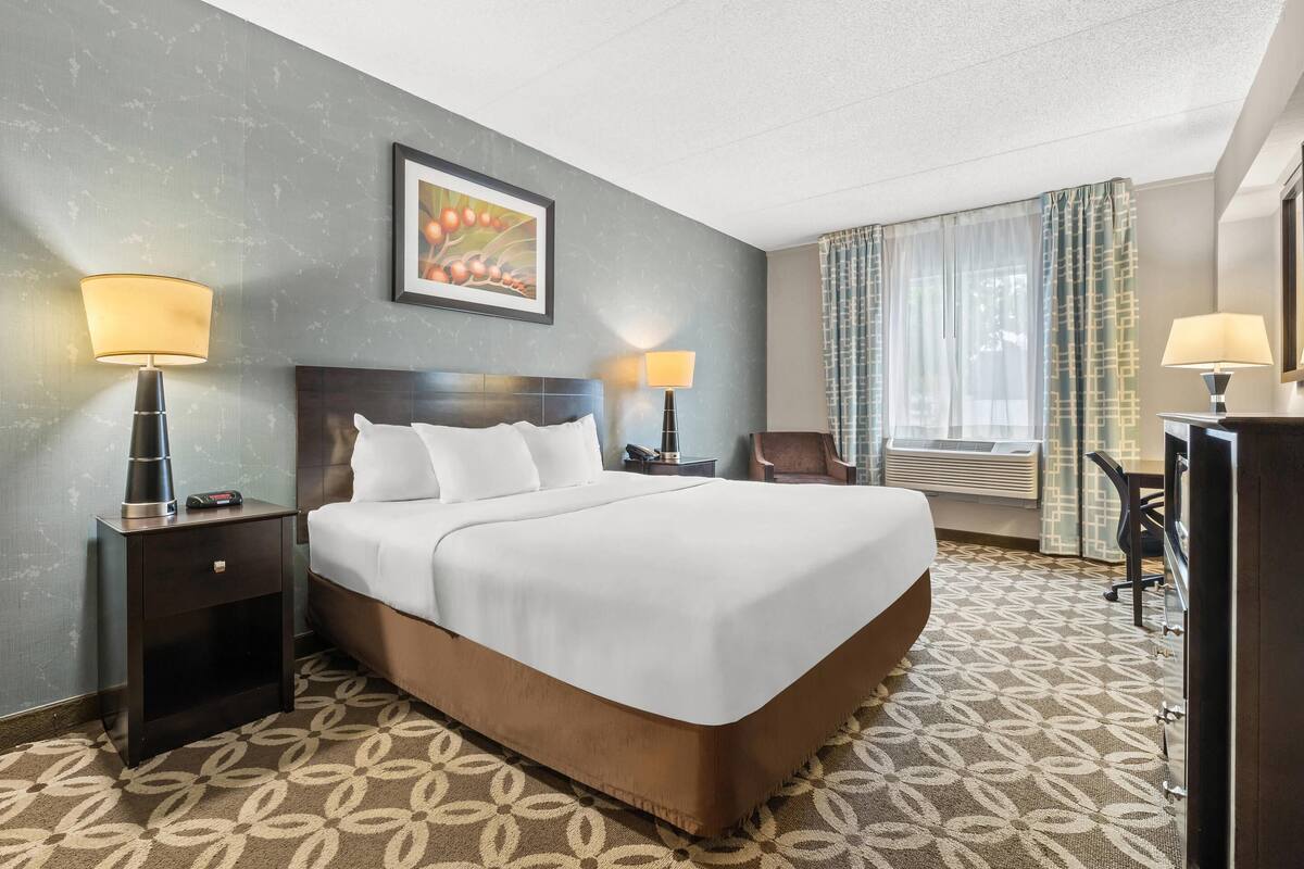 A hotel room with a large bed, two bedside tables with lamps, a chair, and a desk.