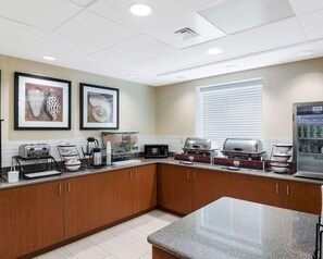 A hotel kitchen with granite countertops, stainless steel appliances, and framed artwork on the wall. - Comfort Inn Rehoboth Beach (Rehoboth Beach)