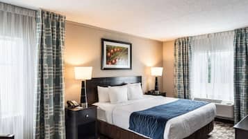 A hotel room with a large bed, two bedside tables with lamps, a framed picture on the wall, and patterned curtains.