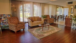 A living room with a sofa, armchair, and coffee table, a dining area with chairs, and a bookshelf with magazines. - Relax Inn Perry (Perry)