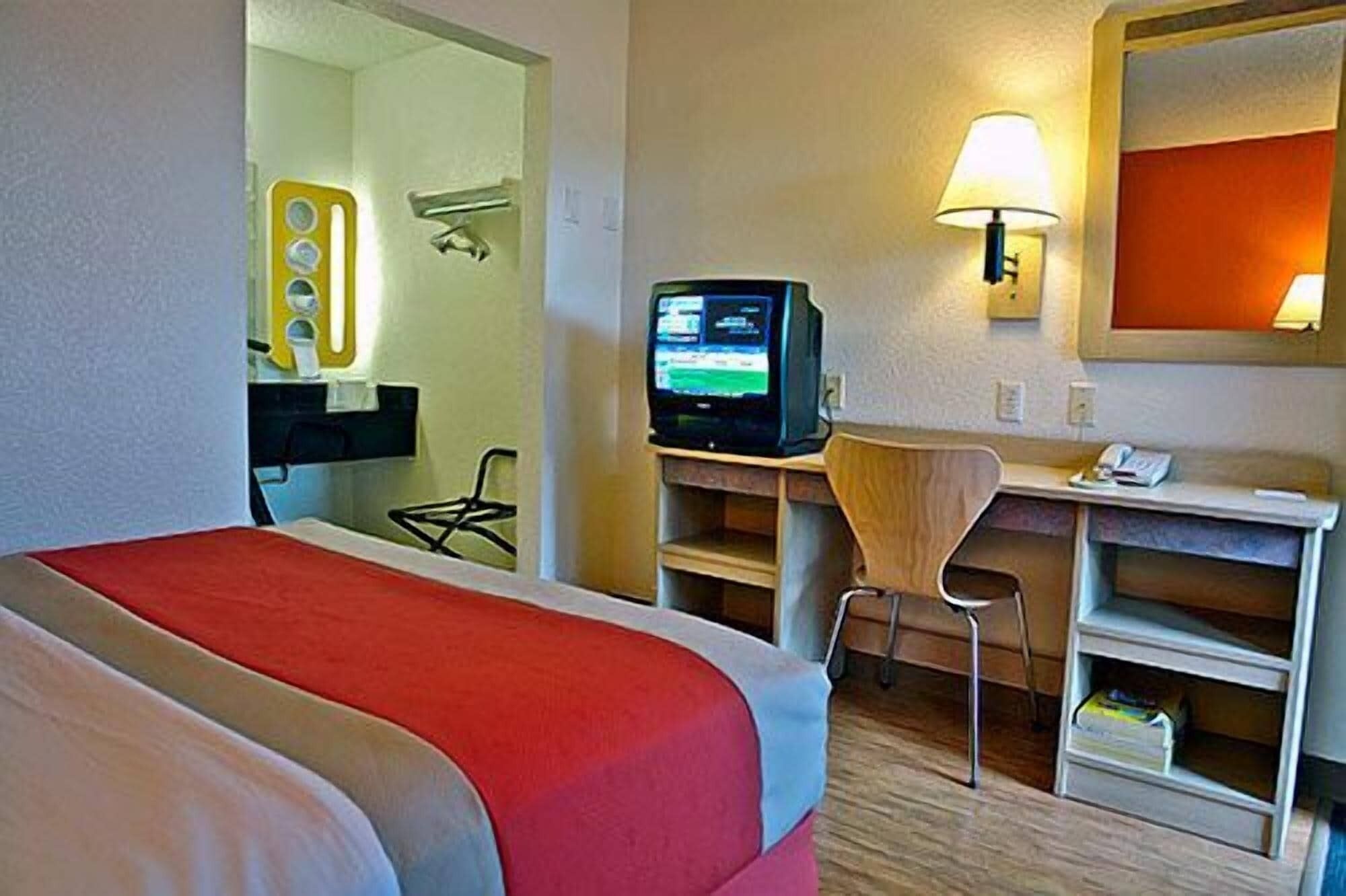 Une chambre d’hôtel équipée d’un lit, d’un bureau avec un ordinateur, d’une chaise, d’une télévision et d’un miroir.