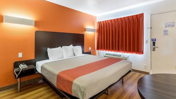 A hotel room with a bed, bedside table, and a desk.