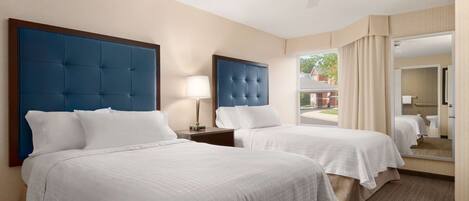 A hotel room with two beds, a ceiling fan, a large mirror, and a view of the outside.