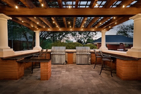An outdoor kitchen with two gas grills, a brick counter, and a pergola with string lights.. Homewood Suites by Hilton Wilmington-Brandywine Valley