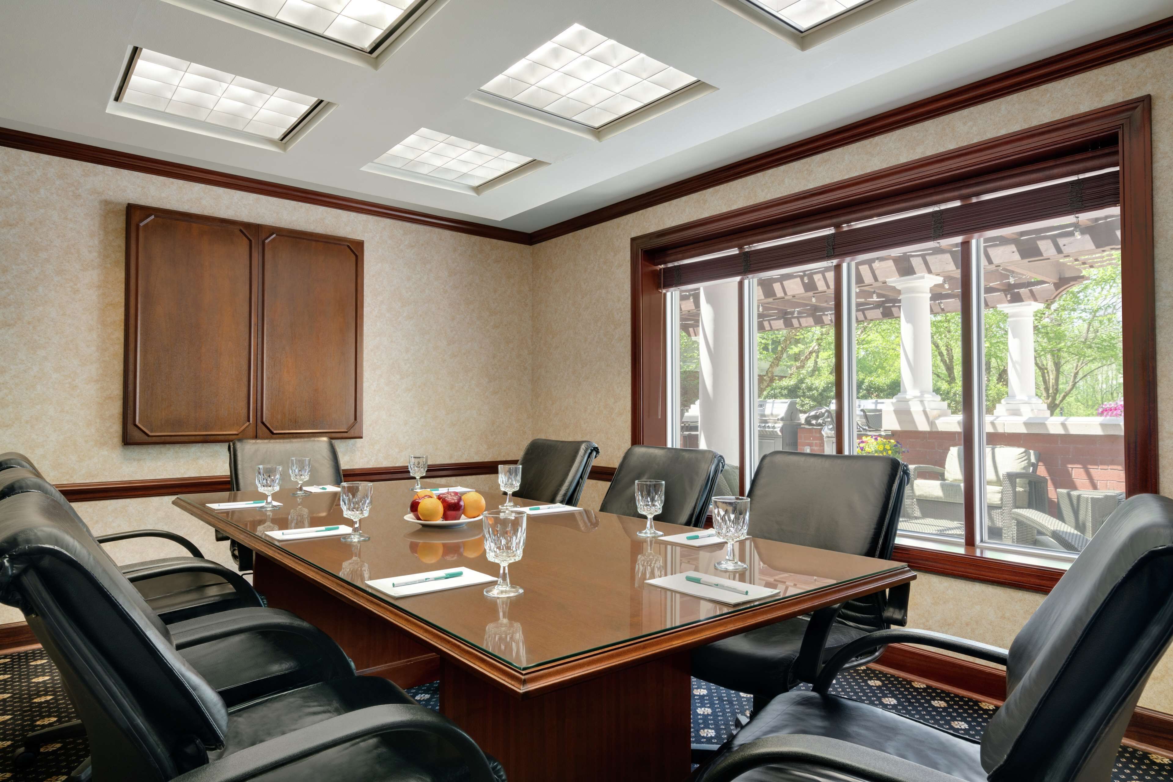 A conference room with a large table, leather chairs, and a view of the outdoors through large windows.