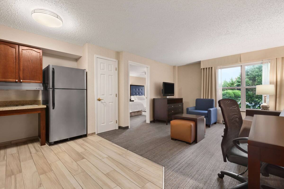 A hotel room with a kitchenette, a bed, a TV, a desk, and a chair.