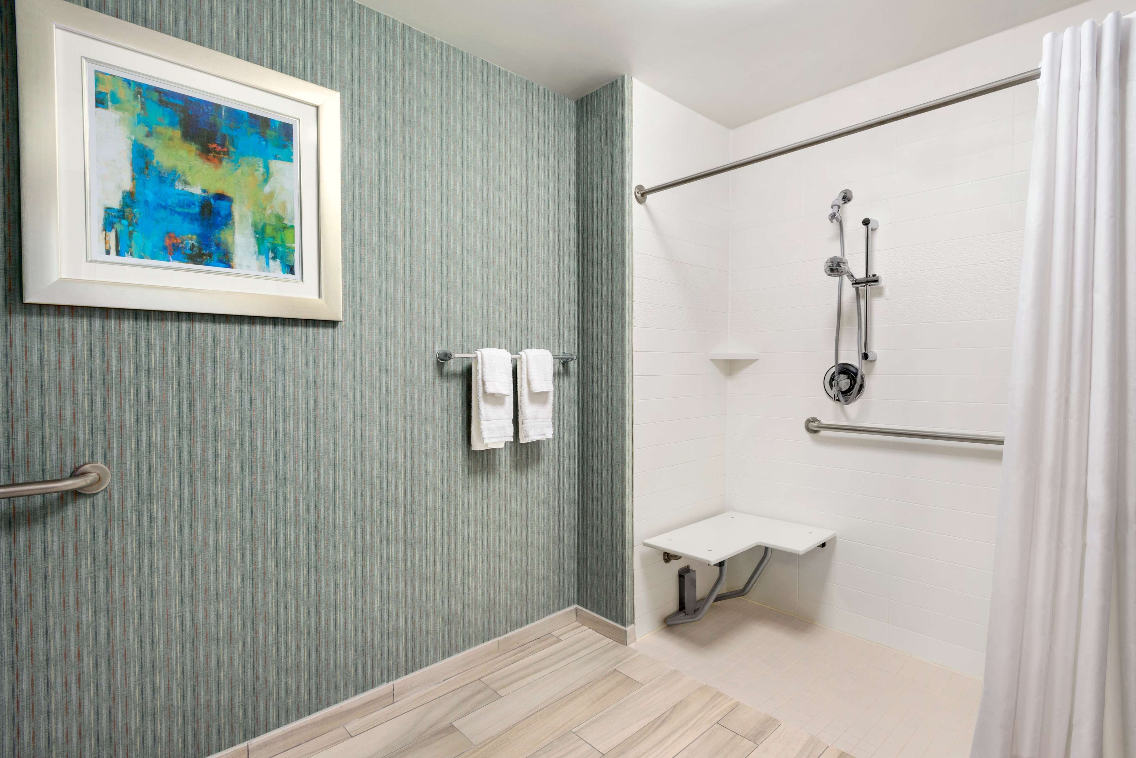 Une salle de bain avec une douche, un tableau abstrait encadré et deux serviettes posées sur un porte-serviettes.