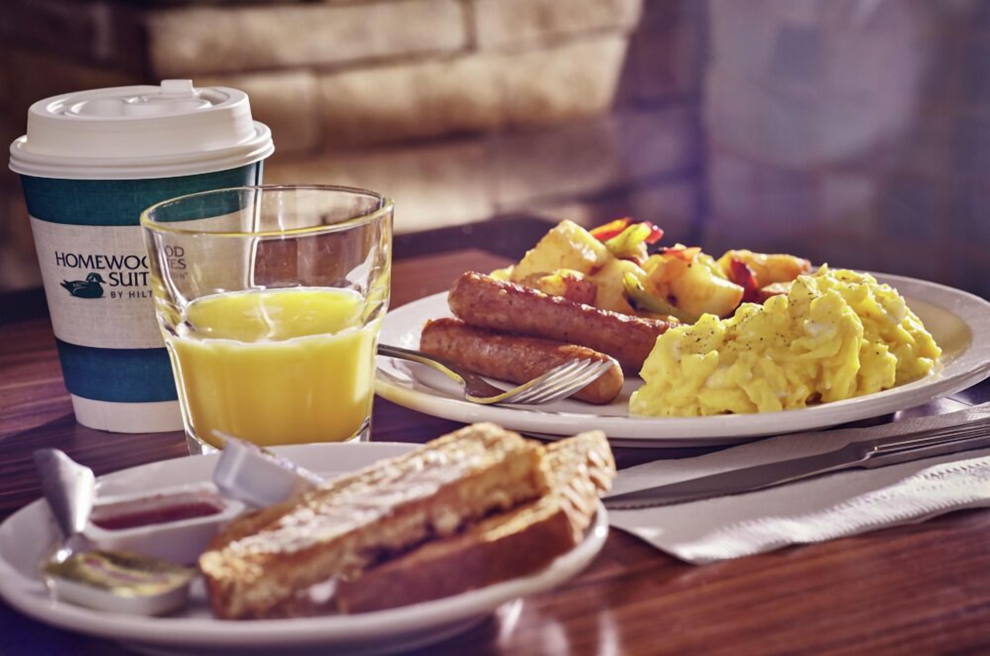 Une table dressée pour le petit-déjeuner avec des œufs brouillés, des saucisses, des toasts et une tasse de café.