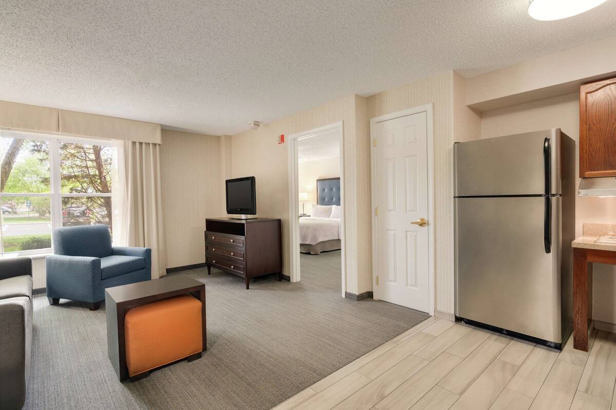 A hotel room with a kitchenette, a TV, a sofa, a small table, and a bed.