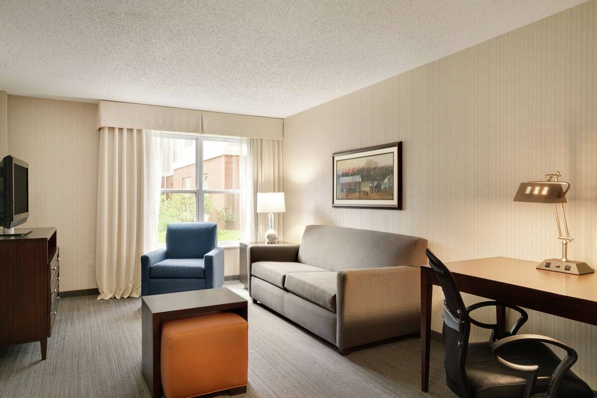 A hotel room with a sofa, armchair, desk, and a television on a dresser.