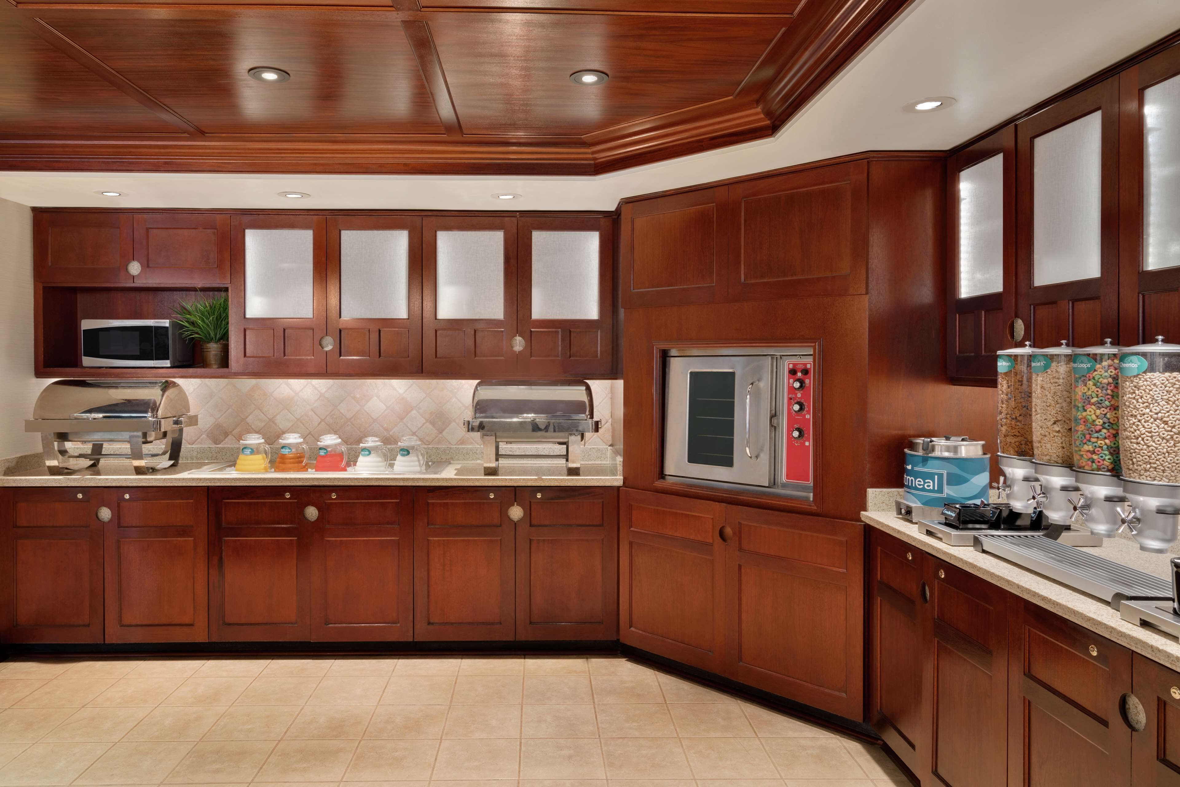 A kitchen with wooden cabinets, a microwave, a grill, a stainless steel oven, and a beverage dispenser.